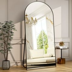 a mirror sitting on top of a wooden floor next to a white couch and potted plant