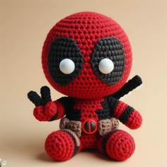 a crocheted deadpool doll sitting on the ground with one hand in the air