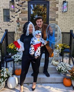 a man and woman holding a baby in front of a house with pumpkins on the steps