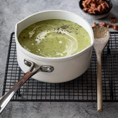 a white bowl filled with broccoli soup on top of a cooling rack next to nuts