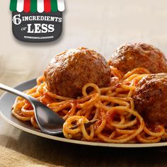 spaghetti and meatballs on a plate with a glass of water in the back ground