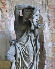 a statue is shown in front of a brick wall and stone pillars, with one person covering his face