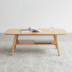 a coffee table with an open book on top and a glass next to it, in front of a white wall