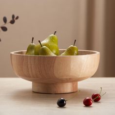 a wooden bowl filled with pears and cherries on top of a table next to a cherry