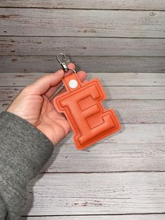 a hand holding an orange leather keychain with the letter e on it