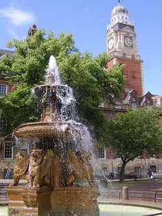 a water fountain in front of a building with a clock tower on the top of it