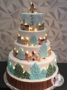 a three tiered cake with lit trees and houses on the top is decorated in white frosting