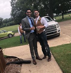 two men standing next to each other in front of a car