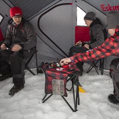 three people sitting in chairs inside of a tent with snow on the ground around them