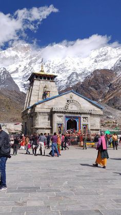 people are walking around in front of a building with snow on the mountains behind it