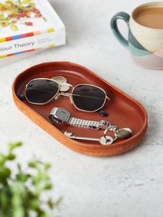 a tray with sunglasses, keys and other items on it next to a cup of coffee