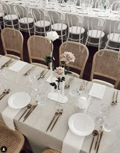 a table set with white plates and silverware, flowers in vases on the tables