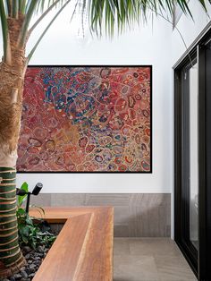 a large painting hanging on the wall next to a wooden bench and palm tree in front of it