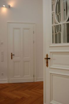 an empty room with wooden floors and white doors, in front of a mirror on the wall