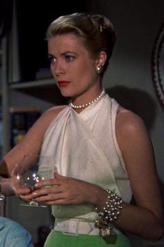 the woman is holding a wine glass in her hand and wearing pearls on her neck