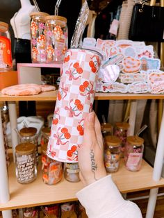 a person holding up a paper cup in front of shelves with candy and candies