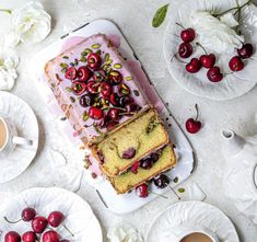 a cake with cherries is on a plate next to some cups and saucers