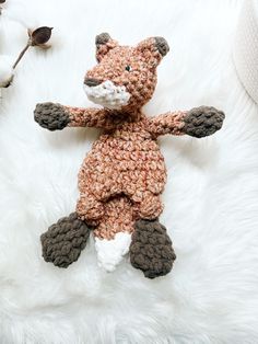 a crocheted stuffed animal laying on top of a white fur covered floor next to a cotton ball