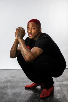 a man sitting on the ground with his hands in front of him and wearing red shoes