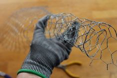 a person wearing gloves and holding a wire mesh object in one hand, with scissors on the other