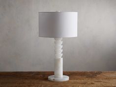 a white table lamp sitting on top of a wooden table next to a gray wall