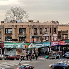 an intersection with cars and people walking on the sidewalk in front of some buildings that are brown