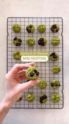 a person holding up a cookie in front of a rack with mini muffins on it