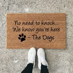 a person standing in front of a door mat that says, no need to knock we know you're here the dogs