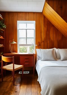 a bedroom with wood paneling and white bedding, wooden desk, and chair