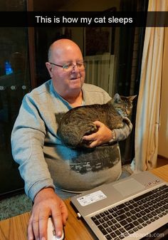 a man sitting at a table with a cat on his lap and a laptop in front of him