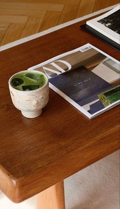 a wooden table topped with a magazine and a cup filled with green liquid next to a laptop computer