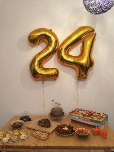 a wooden table topped with lots of desserts and balloon shaped numbers on top of it