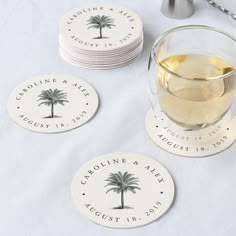 coasters with palm trees on them are sitting next to a glass of white wine