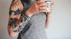 a woman with tattoos holding a coffee cup