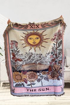 the sun tapestry on display in front of a white couch with flowers and plants around it