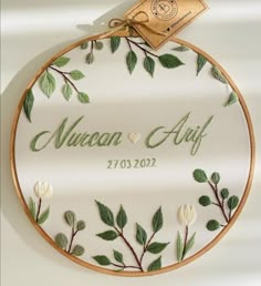 a white embroidered wall hanging with green leaves and the words, nunan & aff on it