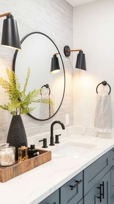 a bathroom sink with two black lamps on the wall and a round mirror above it