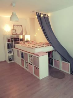 a room with a bed, shelves and a clock on the wall above it that has curtains hanging from the ceiling