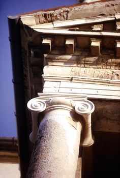 an old column in front of a building with blue sky behind it and no one around