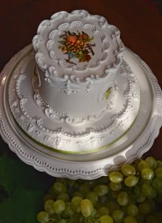 a three tiered white cake sitting on top of a table next to green grapes