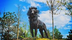 a statue of a lion on top of a hill with trees and bushes around it