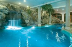 an indoor swimming pool with waterfall and large rocks on the sides, surrounded by water features