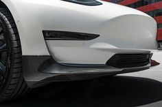 the front end of a white sports car parked in front of a tall red building