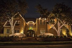 a large house with christmas lights on the front and trees around it's entrance