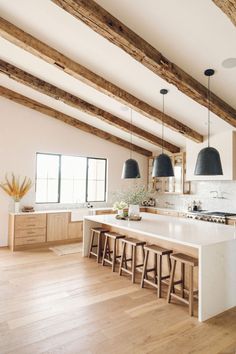 a large kitchen with wooden beams and white counter tops, along with bar stools