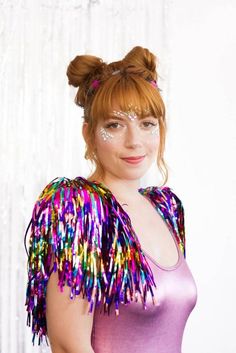 a woman with red hair wearing a purple top and colorful fringes on her shoulders