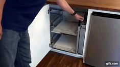 a man is opening the door to an empty dishwasher in a kitchen with wood flooring