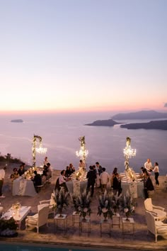 a group of people sitting at tables on top of a hill next to the ocean