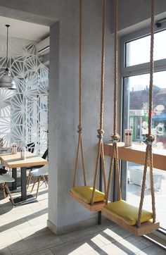 two yellow swings are hanging from the ceiling in front of a large window and table with chairs