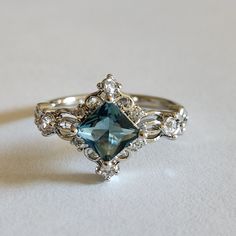 a fancy ring with an aqua blue stone surrounded by white diamonds on a plain surface